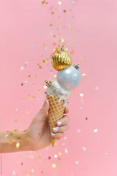 a hand holding an ice cream cone with gold and silver decorations on top by jodi lenski for stocksy photography