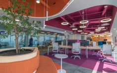 an office with pink and orange walls, white desks and plants in the center