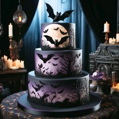 a three tiered halloween cake with bats on top and candles in the back ground