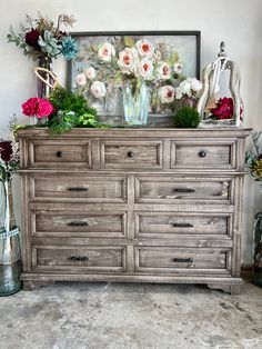 an old dresser with flowers and vases on top