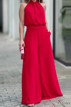 a woman in a red jumpsuit is standing on the sidewalk with her hands behind her back