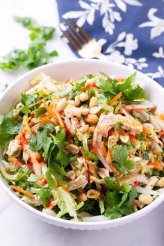 a white bowl filled with salad and garnished with cilantro, carrots, cashews and peanuts