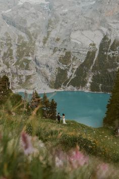 a bride and groom standing on top of a grass covered hill next to a lake