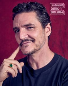 a man with a ring on his finger posing for a photo in front of a red background