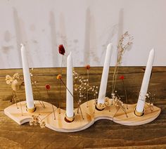 four white candles are placed on a wooden stand with dried flowers in the center and one is turned upside down