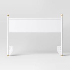 a white bed frame with two gold posts on the top and bottom, against a gray background