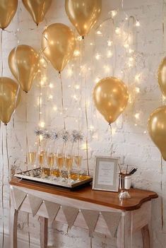 gold balloons are hanging from the ceiling above a table with champagne glasses and an empty tray on it