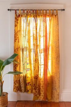 a yellow curtain hanging in front of a window next to a potted plant on top of a wooden floor