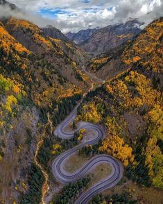 an aerial view of a winding road surrounded by trees and mountains in the fall season