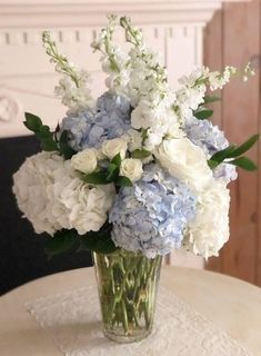 a glass vase filled with blue and white flowers on top of a table next to a fireplace