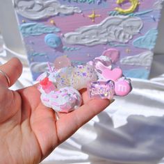 a hand is holding some small toys in front of a box with clouds and stars on it