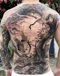 a man with tattoos on his back is standing in front of some trees and birds