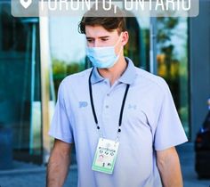 a man wearing a face mask and lanyard walking down the street in front of a building