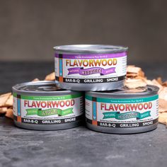 three cans of flavored dog food sitting on top of each other next to wood chips