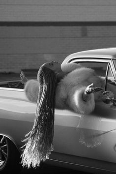 a woman is sitting in the back of a car with her hair hanging from it's roof