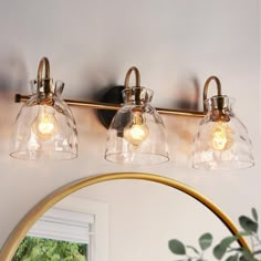 three light bathroom fixture with clear glass shades and brass finish, on a white wall