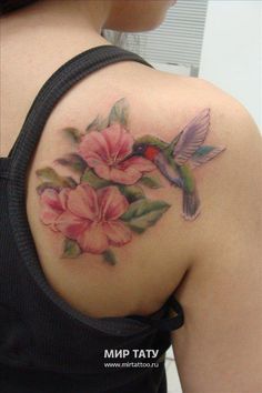 a woman's back with flowers and a hummingbird tattoo on her left shoulder