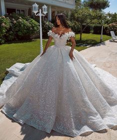 a woman in a white wedding dress standing on the ground near some grass and trees