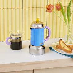 a blue coffee pot sitting on top of a counter next to a plate with bread