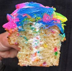 someone holding up a piece of cake with sprinkles and frosting on it