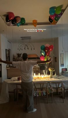 a man standing in front of a birthday cake with candles on it and balloons hanging from the ceiling