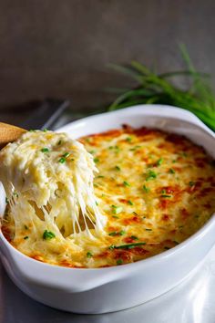 a wooden spoon scooping some food out of a casserole dish with cheese and chives