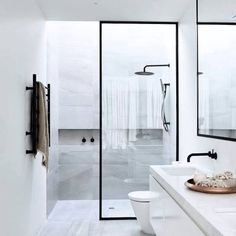 a white bathroom with two sinks, mirrors and a shower stall in the middle of the room