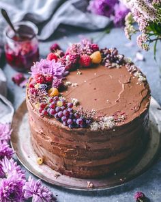 there is a chocolate cake with berries on it and purple flowers around the edges,