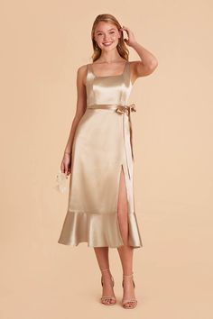 a woman wearing a champagne colored dress with a slit down the side and a tan sash around her waist