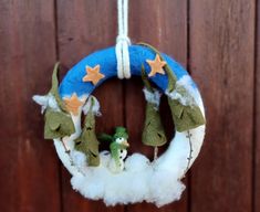 a blue wreath with snowmen and trees hanging from it's side on a wooden fence