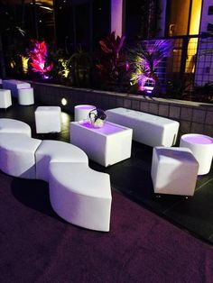 an outdoor seating area with white chairs and purple rugs on the ground at night