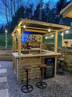 an outdoor bar with stools and lights on the outside wall, in front of a grassy area