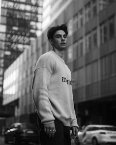 a man standing in front of a tall building wearing a sweatshirt with the word esttia on it