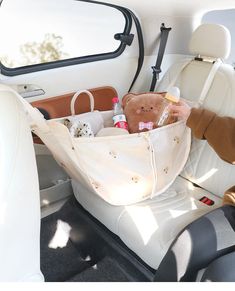 a baby in a car seat holding a teddy bear and diaper bag with the door open