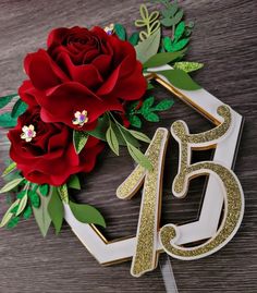 a red rose sitting on top of a wooden table next to a white and gold number