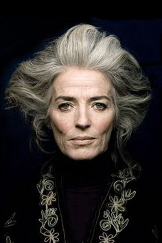 an older woman with grey hair and black shirt looking at the camera, in front of a dark background