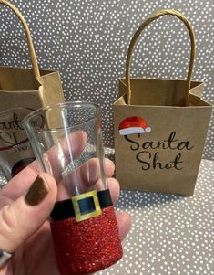 a hand holding a small glass with santa hat on it next to a brown paper bag