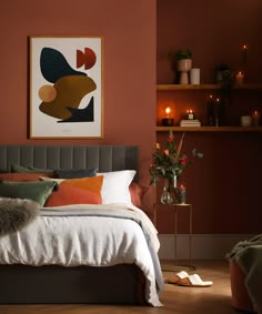 a bed in a bedroom with red walls and orange pillows on the headboard, next to a plant