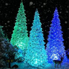 christmas trees are lit up in blue and green lights, with snow falling on them