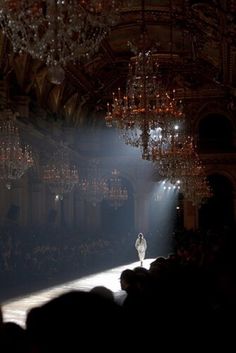 chandelier hanging from the ceiling in front of a runway with a woman walking down it