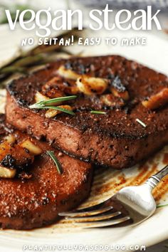 two pieces of steak sitting on top of a white plate next to a fork and knife