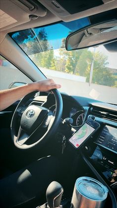 a person driving a car with their hand on the steering wheel, while holding an electronic device