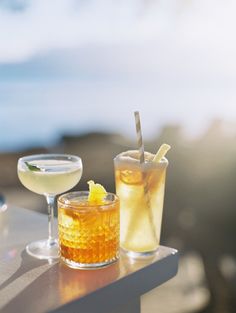 two drinks sitting on top of a table next to each other near the ocean and sky