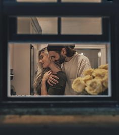 a man and woman embracing each other in front of a window