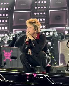 a man sitting on top of a stage with his hands to his face as he covers his mouth