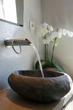 a bowl shaped sink sitting on top of a wooden table next to a vase with white flowers