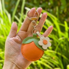 a hand holding an orange keychain with a flower on the front and side