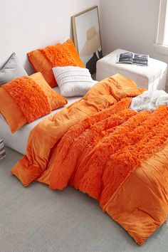 an orange comforter on a bed in a room with white walls and flooring