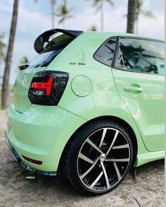 the rear end of a green car parked on top of a sandy beach next to palm trees