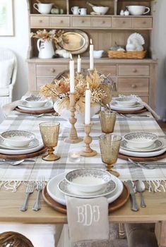 a dining room table set with plates and silverware, candlesticks and napkins